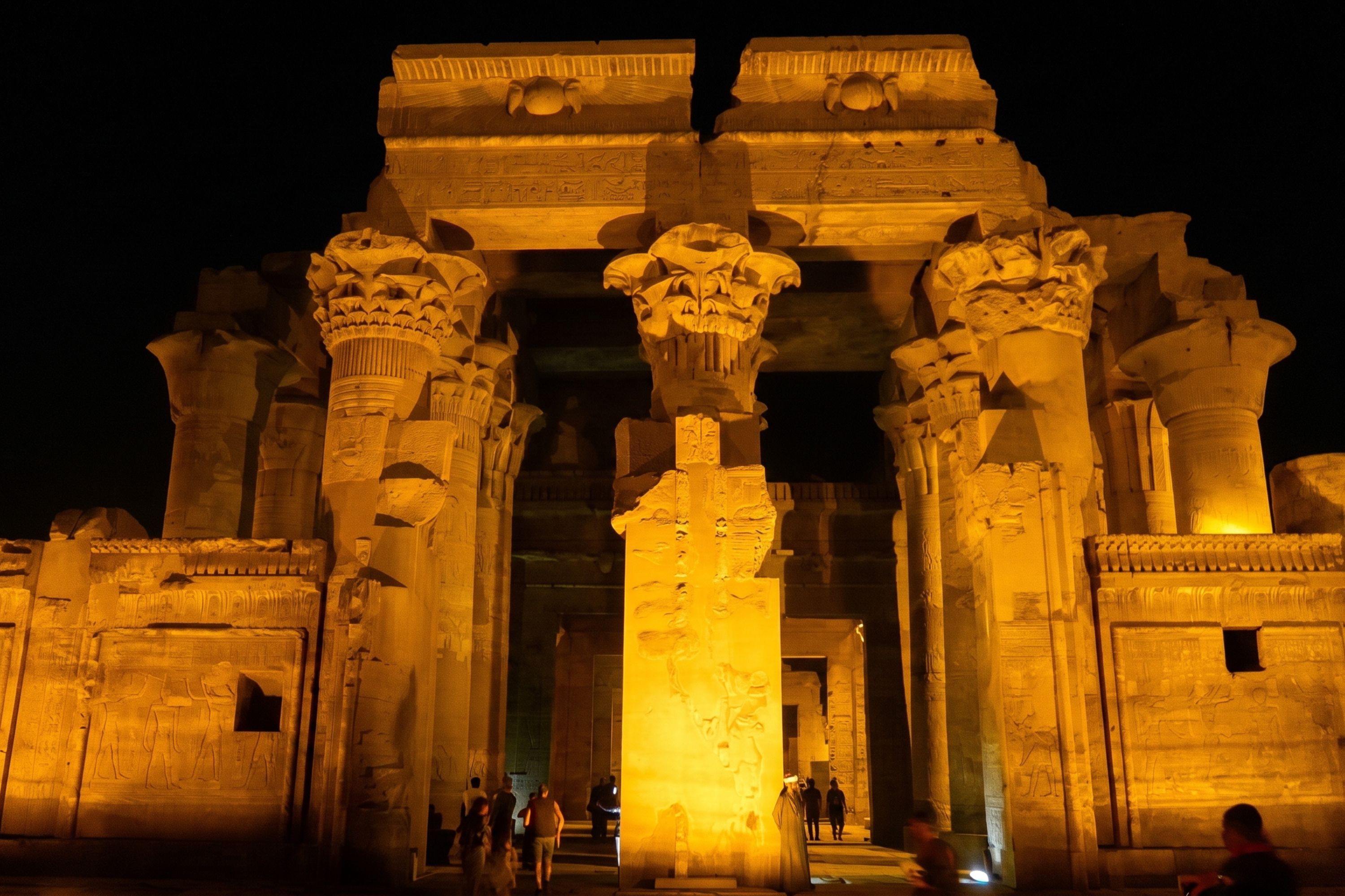 Ancient Egyptian temple columns and carved stone walls illuminated in golden light at night.