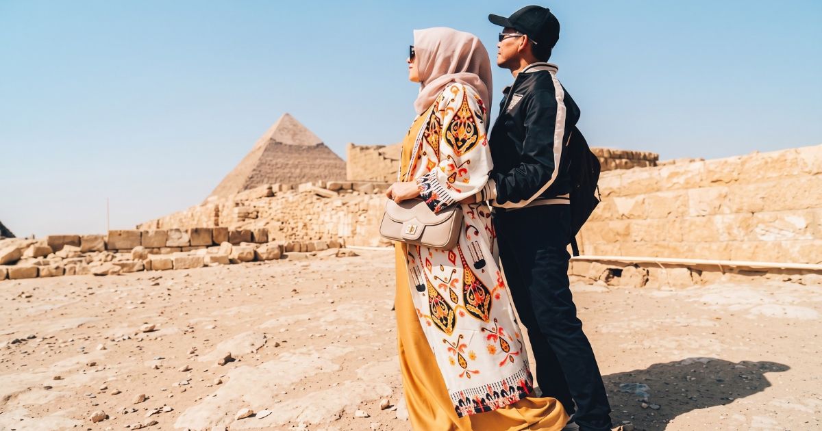 A couple walking together at the Giza pyramid complex in Egypt, with a pyramid and ancient stone ruins behind them