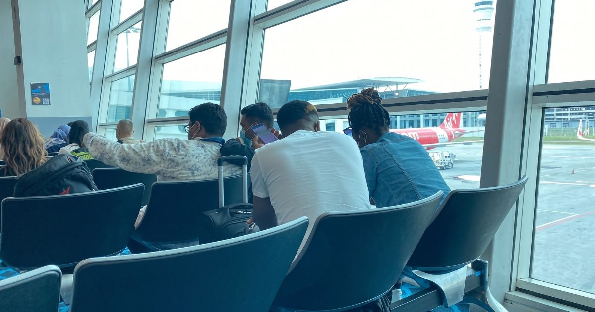 Travellers waiting with luggage in an airport terminal, watching a plane on the tarmac