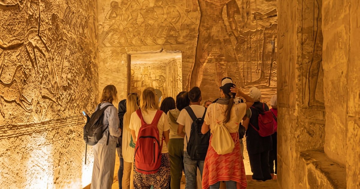 A traveller walking with an Egyptian guide past souvenir stalls and an ancient columned building in Luxor